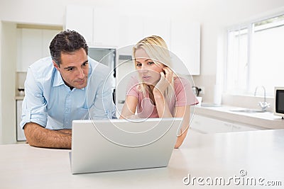 Concentrated couple using laptop in kitchen Stock Photo