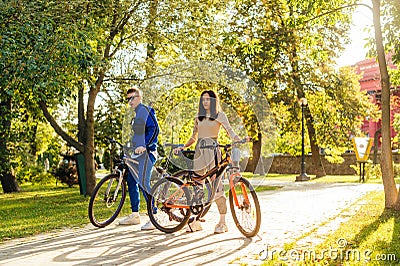 Concentrated couple of young cyclists is riding bicycles in the city park on a sunny summer day. Man and woman in colorful casual Stock Photo