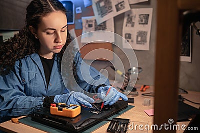 Concentrated female technician busy repairing laptop and it testing with multimeter at retro workshop. professional Stock Photo
