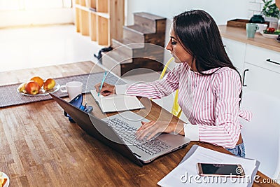 Concentrated freelancer woman making notes from internet working home sitting at table Stock Photo
