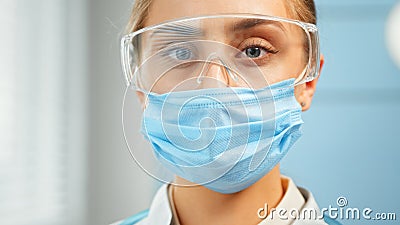 Concentrated lady doctor in blue disposable facial mask and protective goggles looks straight Stock Photo