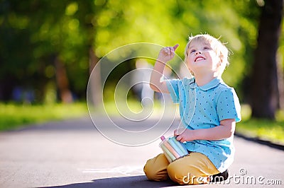 Concentrated little kid boy sitting and drawing with colored chalk on asphalt Stock Photo