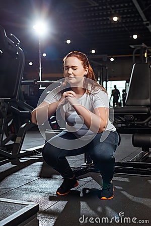 Concentrated overweight girl with closed eyes squatting with clenched hands Stock Photo