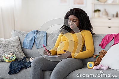 Concentrated pregnant woman sitting on sofa with notebook and pen Stock Photo