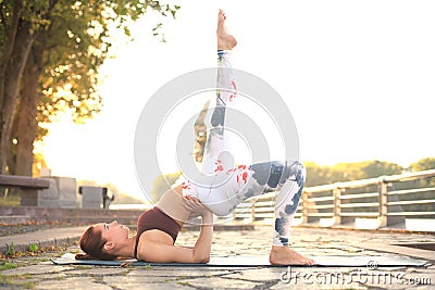 Concentrated pretty strong young redhead sports woman make yoga exercise outdoors Stock Photo