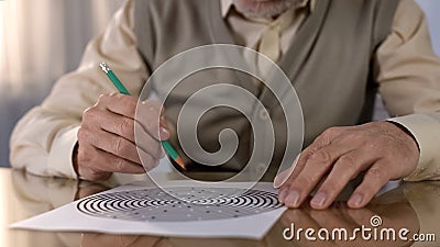 Concentrated retired man solving logic test at table, memory exercise, neurology Stock Photo