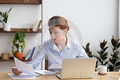 Concentrated serious young woman working with business document and laptop Stock Photo