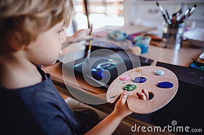 Concentrated small boy painting pictures indoors at home, leisure time. Stock Photo