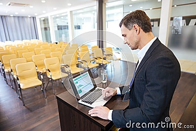 Concentrated speaker standing at tribune and using laptop Stock Photo