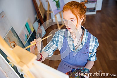 Concentrated woman painter holding art palette and painting on canvas Stock Photo