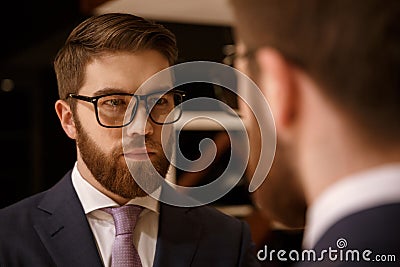 Concentrated young bearded businessman looking at mirror. Stock Photo