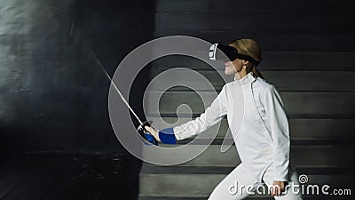 Concentrated fencer woman practice fencing exercises using VR headset and training simulator competition game indoors Stock Photo