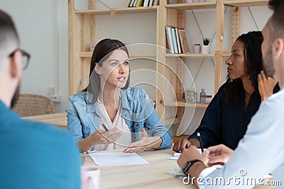 Concentrated young mixed race colleagues listening to female team leader. Stock Photo