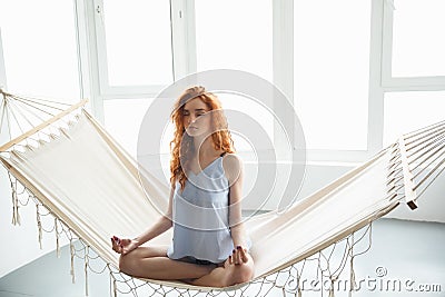 Concentrated young redhead lady sitting on hammock meditate Stock Photo