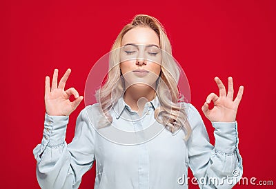 Concentration and enjoying. Young woman with closed eyes shows excellent sign with finger while enjoying, isolated on red Stock Photo