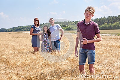 Concept of adopted kid, boy standing on foreground with adoptive family on background, stepson with dad, mom and preteen sister Stock Photo