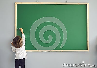 Concept back to school. Back view. Little schoolboy writes on a school board in a school class. Stock Photo