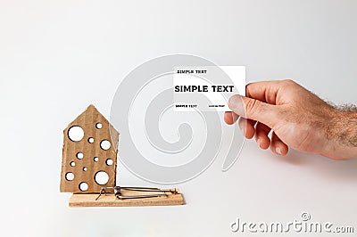 Concept of Bank investments and risks. A man`s hand holds a Bank card, and next to it is a big mousetrap with a cardboard house Stock Photo