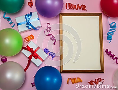 Wooden photo frame, multicolored streamer, gift boxes and balloons on a pink background. Stock Photo