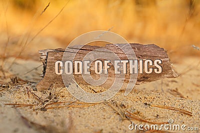 In the sand against the background of yellow grass there is a sign with the inscription - CODE OF ETHICS Stock Photo