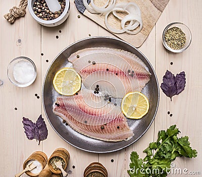 concept cooking tilapia fillets with lemon on vintage pan with herbs, vegetables and spices on wooden rustic background top view Stock Photo