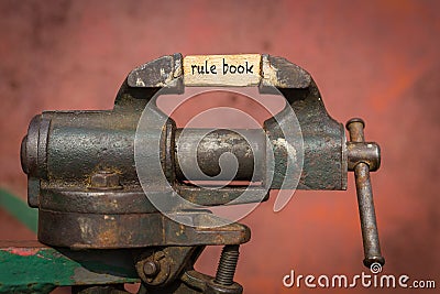 Vice grip tool squeezing a plank with the word rule book Stock Photo