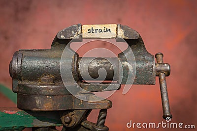 Vice grip tool squeezing a plank with the word strain Stock Photo
