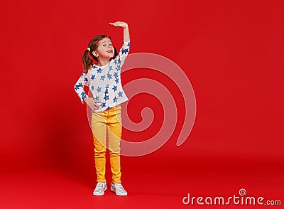 Concept of development and growth, kid girl measuring height on red colored background Stock Photo