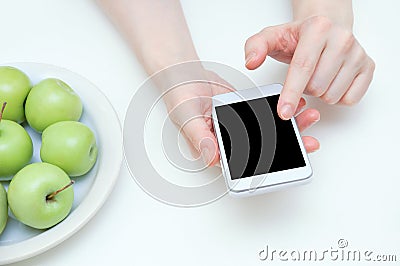 The concept of diet. A smartphone in the hands of a Caucasian girl and a plate of apples on the table. Stock Photo