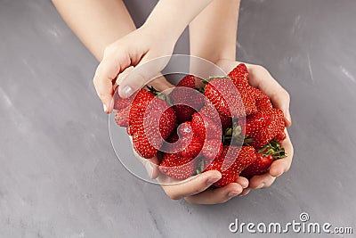 Concept - Eating ugly fruits and vegetables. Children`s hand takes a ripe funny strawberries of unusual shape from female hands. Stock Photo