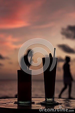 Silhouette of two cocktail during sunset in a tropical island. people passing by in the background. Happy Hour Stock Photo
