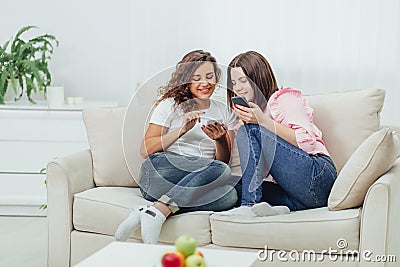 Two roommates using their smartphones at home sitting on a sofa in the living room. Stock Photo