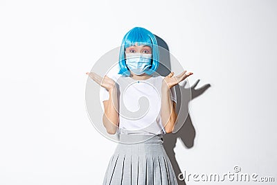 Concept of halloween celebration and covid-19 pandemic. Image of cute asian girl having fun, wearing blue wig and Stock Photo