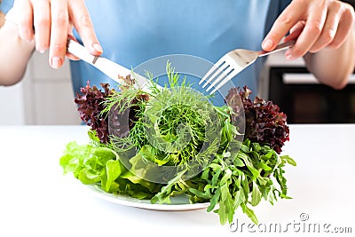 The concept of a healthy, balanced, dietary food. Girl with knife and fork eating fresh vitamin green salad. Stock Photo