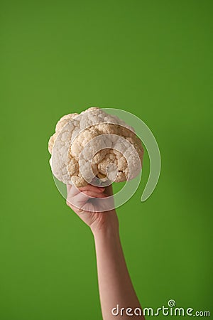 Female hand holds cauliflower on a green background. The concept of veganism and vegetarianism. Stock Photo