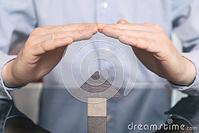 Concept home insurance, protection from burglary or destruction. Man with his hands covers the hous of wood Stock Photo