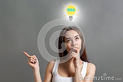 Concept of idea and information search. Portrait of a pensive young Caucasian woman, with an idea sign above her head, pointing Stock Photo