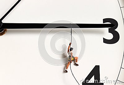 A miniature climber hanging by a rope on a black watch needle. Stock Photo