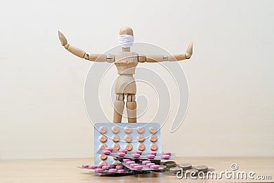 One wooden man mannequin in a protective medical mask holds his hands in different directions standing near a pile of medicine ta Stock Photo