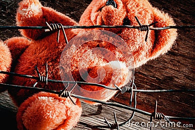 Concept: lost childhood, loneliness and pain. Dirty teddy bear behind barbed wire Stock Photo