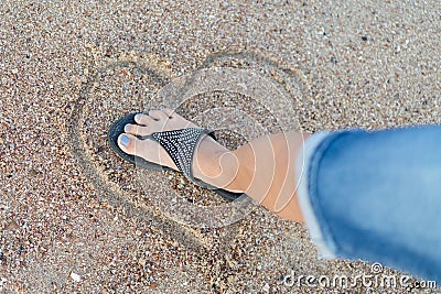 The concept of loveless love and a broken heart. Female foot crushes a heart made of sand Stock Photo