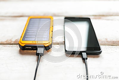 Concept of modern technologies and power bank. Smartphone charged from a portable solar charger. White wooden background with Stock Photo