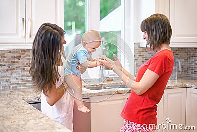 The concept of motherhood, nanny, infancy and childhood. Indoor shot in the kitchen. Two women and a baby in their arms Stock Photo