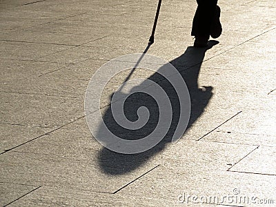 Person walking with a cane, black silhouette and long shadow on pavement Stock Photo