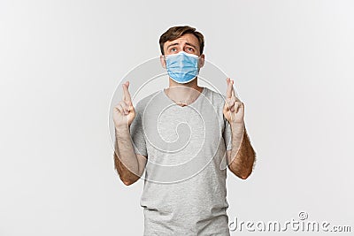 Concept of pandemic, covid-19 and social-distancing. Hopeful worried guy in medical mask, cross fingers for good luck Stock Photo