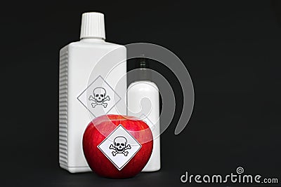 Concept of pesticide residues in agricultural food products showing a red apple and white bottles with poison symbol sticker on bl Stock Photo