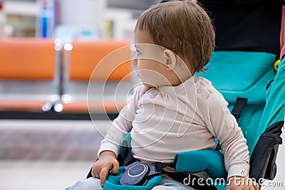 Concept pf travel vith children. Little cute baby girl sitting in a stroller and carefully looking to the side. in the Stock Photo