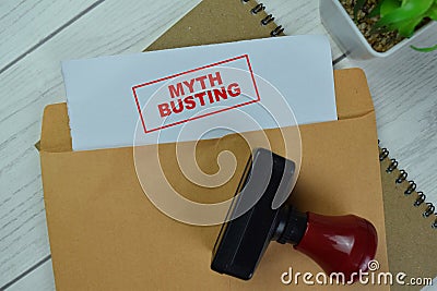 Concept of Red Handle Rubber Stamper and Myth Busting text above Brown envelope isolated on on Wooden Table Stock Photo