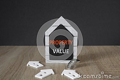 Concept red words Property value on a black board in the shape of a house near miniature houses. Beautiful wooden table. Business Stock Photo