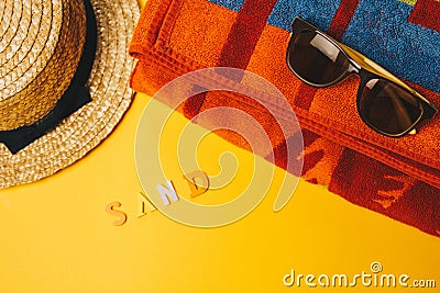 Concept of relaxing on the beach. inscription sand on a yellow background with sunglasses, a towel and a straw hat. top view Stock Photo